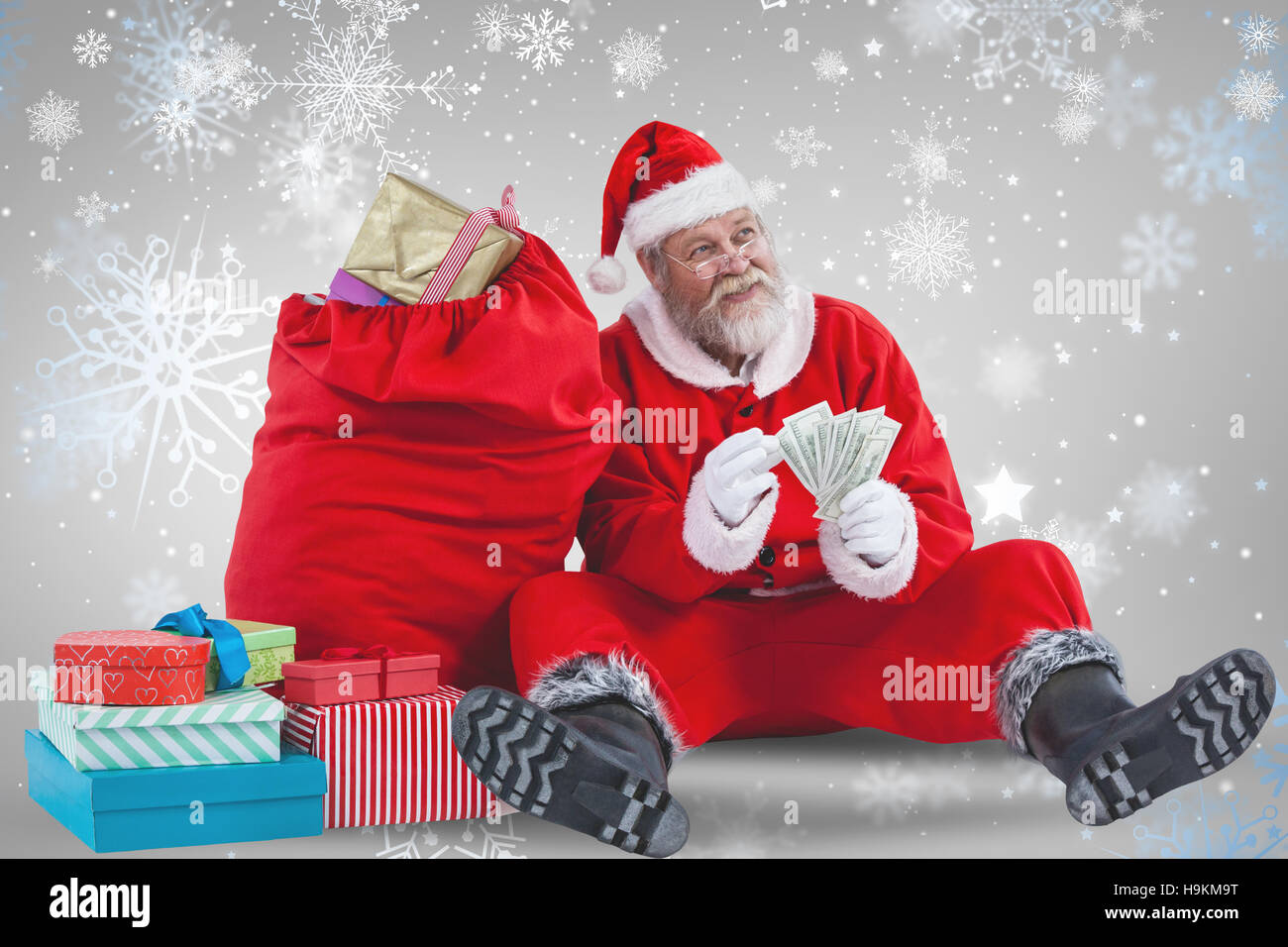 Composite image of santa claus sitting by christmas gifts counting bills Stock Photo