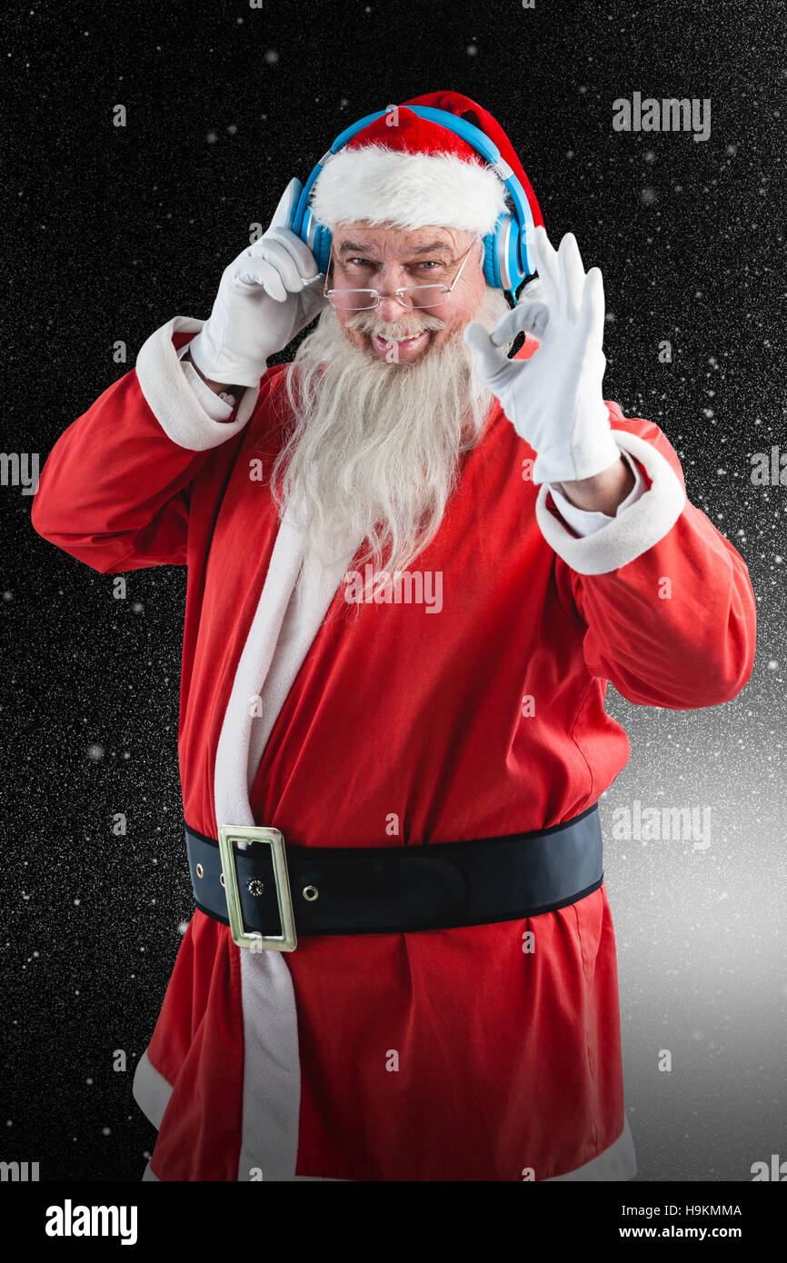 Composite image of santa claus showing hand okay sign while listening to music on headphones Stock Photo