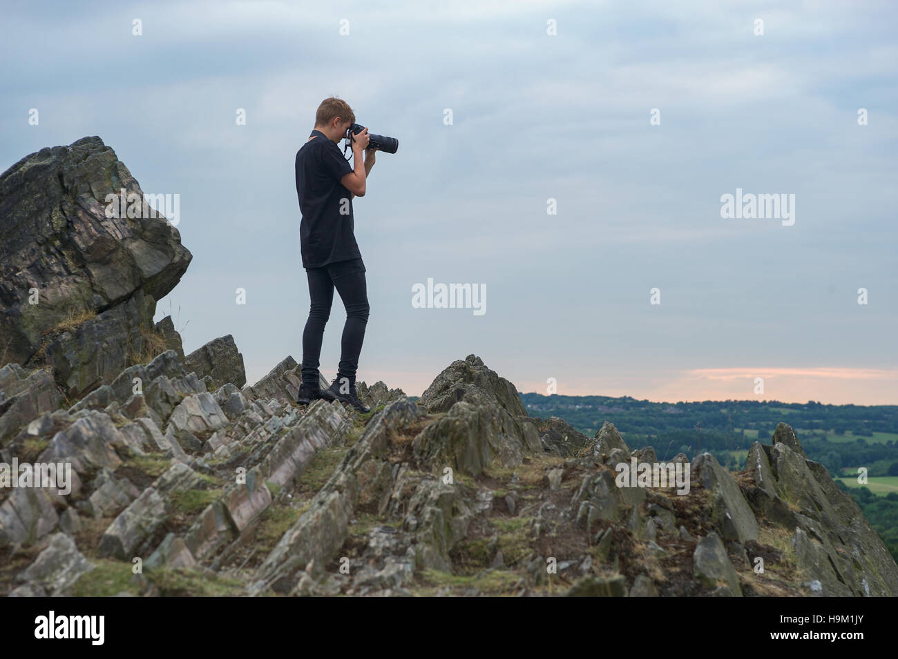A young photographer takes a photo on a rocky ridge. Stock Photo