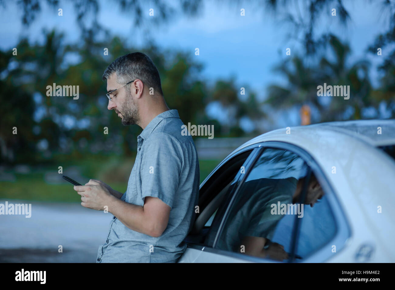 Man using smart phone GPS leaning against his car Stock Photo