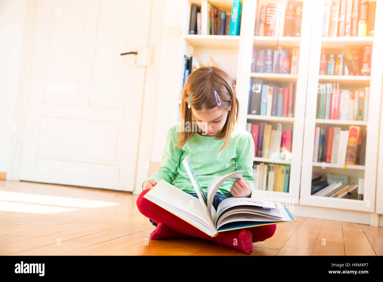 Little girl sitting on the floor watching turning pages of a book Stock ...