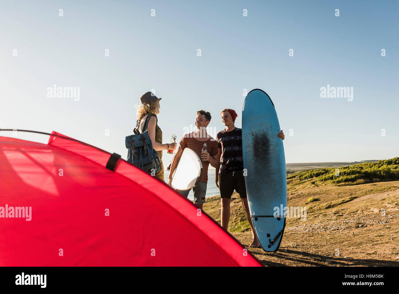 Three friends with surfboards camping at seaside Stock Photo