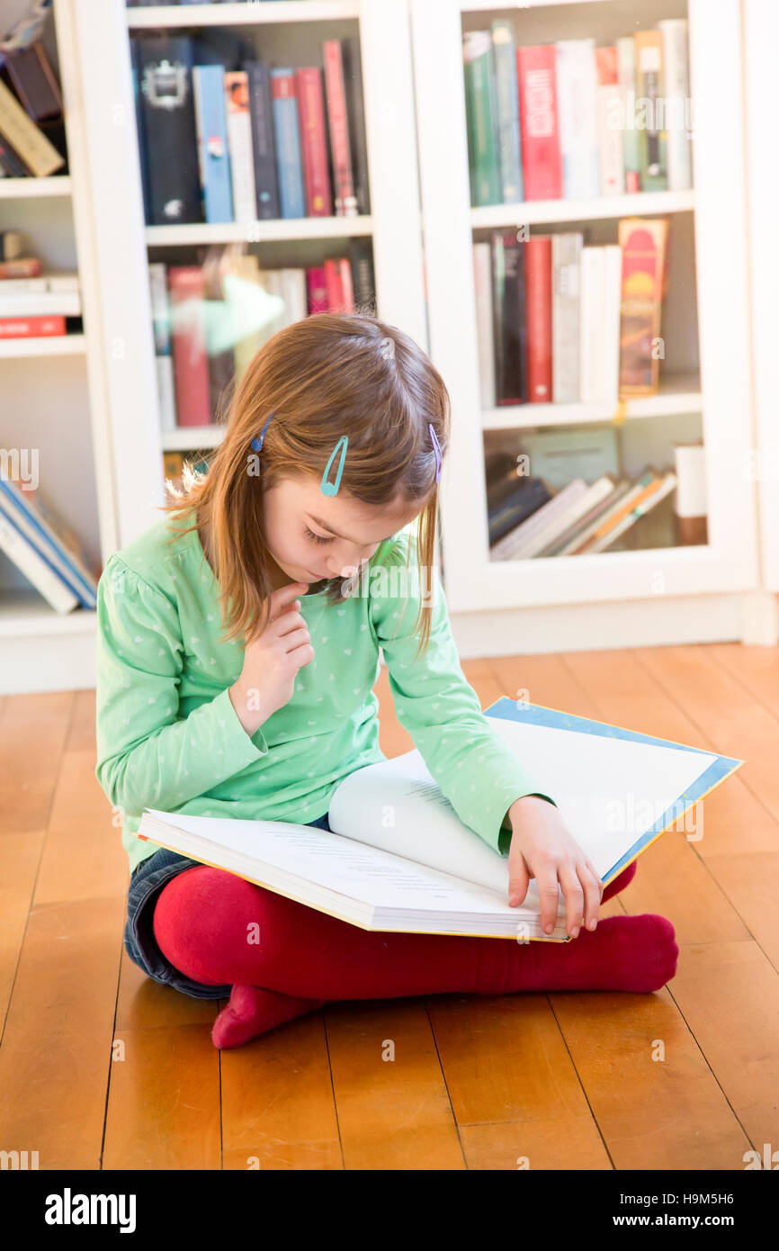 Little girl sitting on the floor reading a book Stock Photo - Alamy