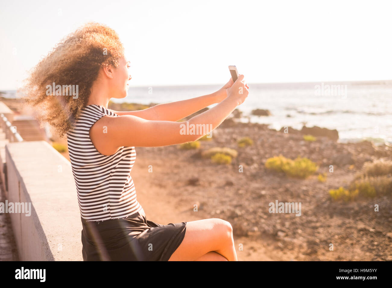 Woman sitting on a wall taking picture of the sea Stock Photo - Alamy
