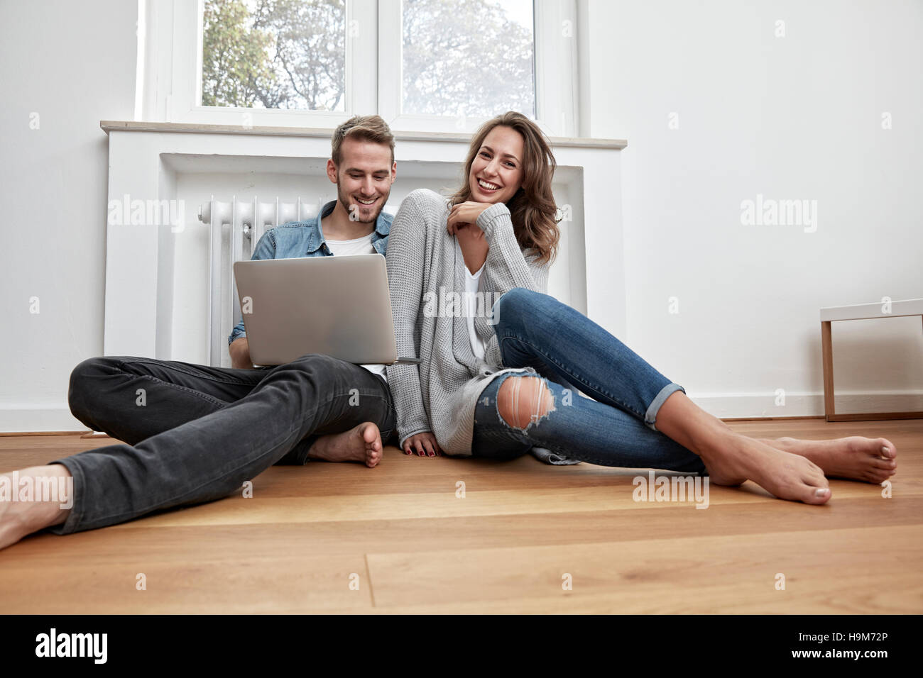 Smiling couple sitting on the floor with laptop Stock Photo - Alamy