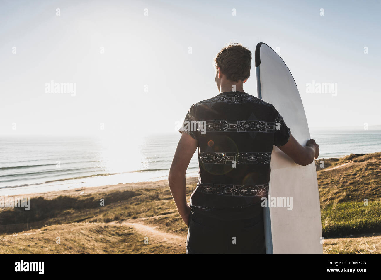 Back view of teenage boy with surfboard looking to the sea Stock Photo