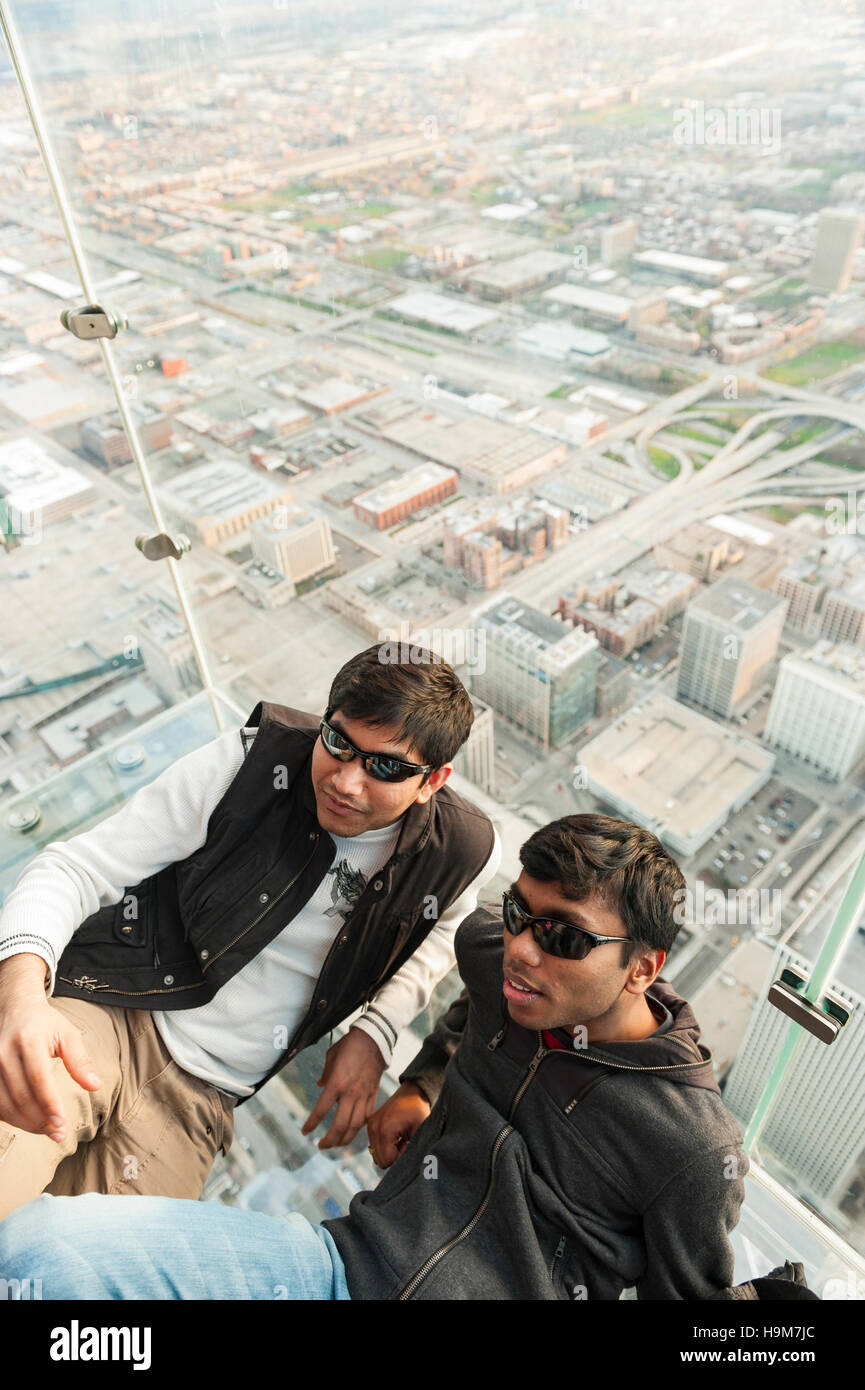 Two young minority men wearing sunglasses laying on the glass floor of the Skydeck observation floor of Willis Tower in Chicago, Illinois, USA Stock Photo