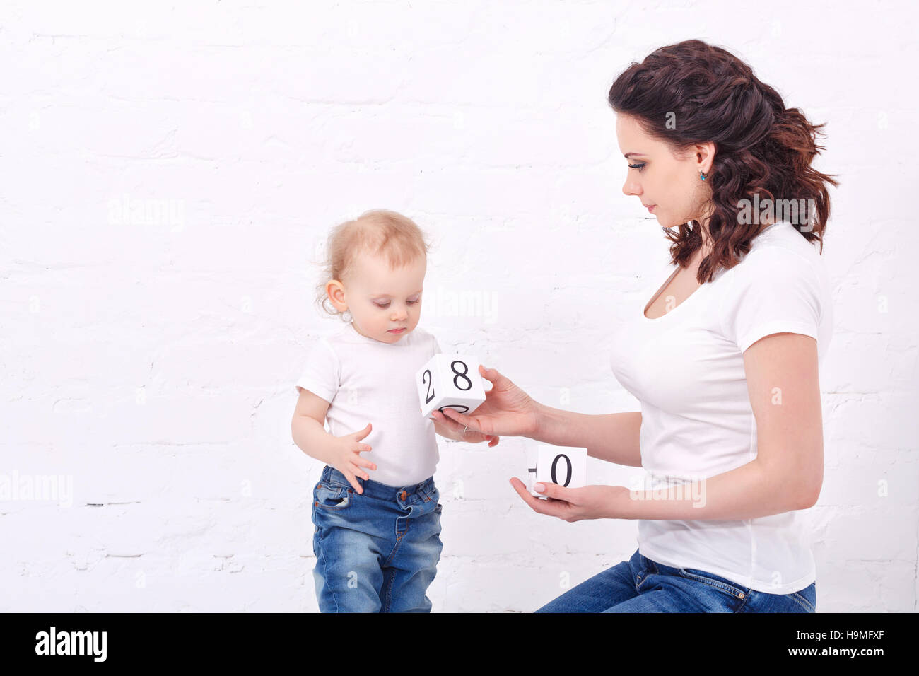 Mother and daughter playing with blocks. On the dice have numbers. Family education. Mother and daughter dressed in jeans and white T-shirts. Family Stock Photo