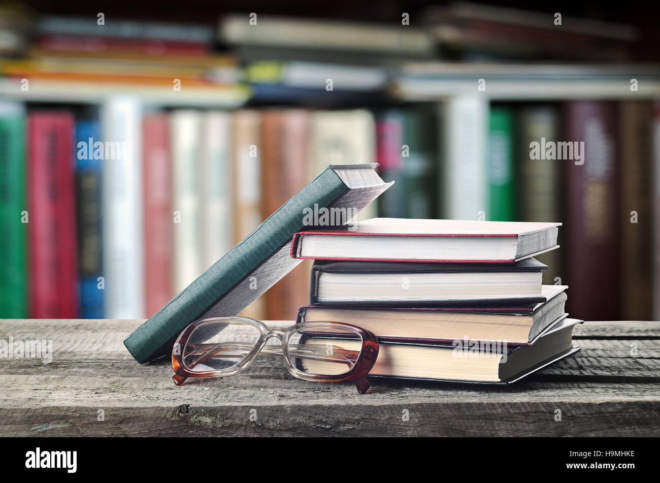 Stack of books and glasses on wooden table with bookshelf, invitation to study literatures, close up, reading room Stock Photo