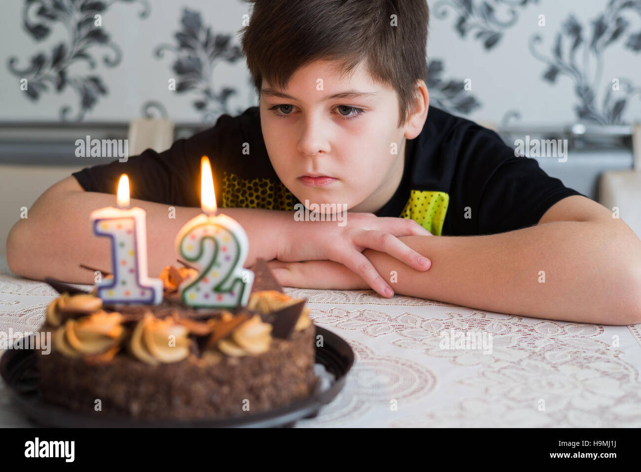 Teen boy looks thoughtfully at cake with candles on twelfth day of birth Stock Photo