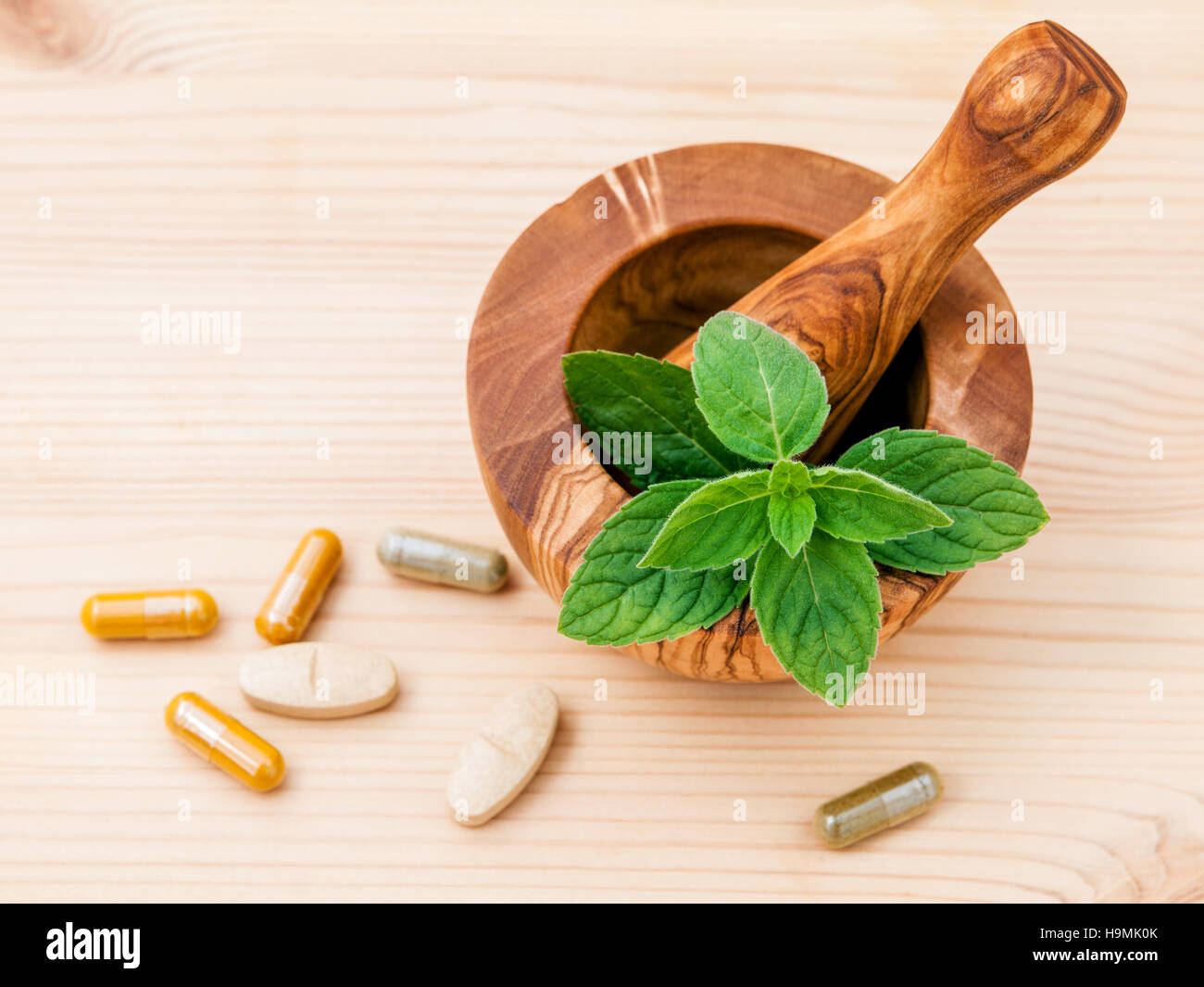 Fresh peppermint leaves in olive wood mortar and capsule of herbal medicine . Alternative health care concept setup on wooden ba Stock Photo