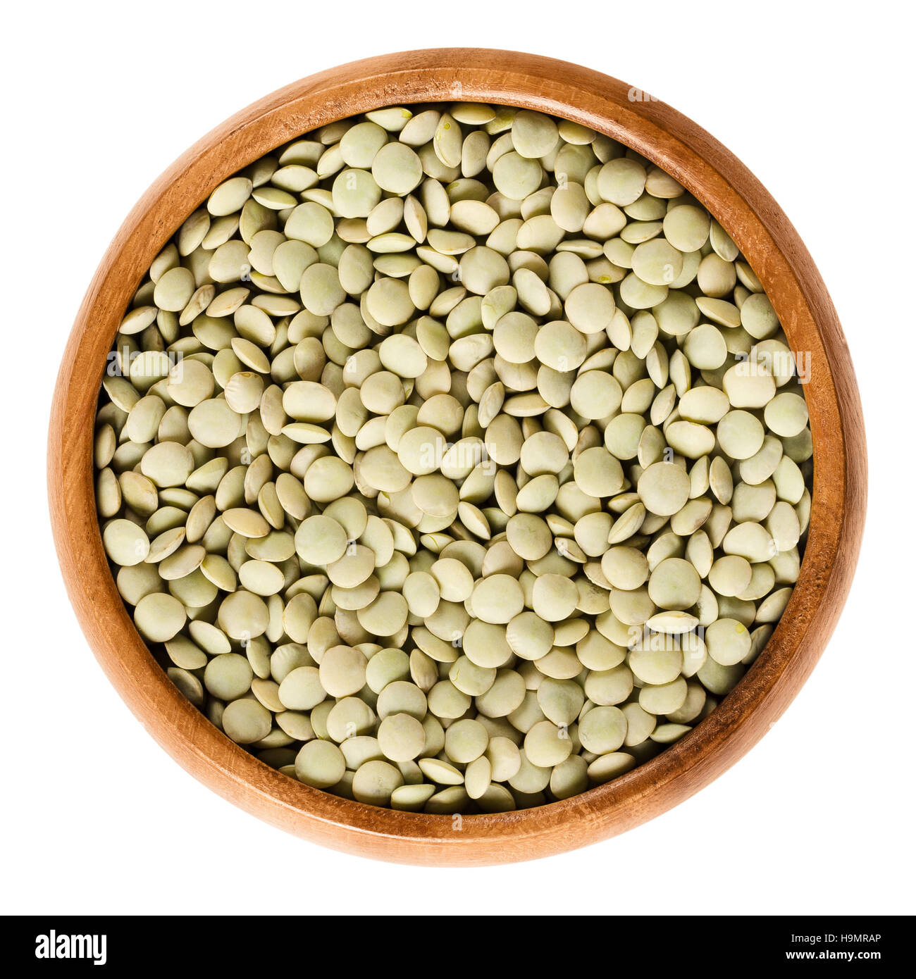 Green lentils in wooden bowl on white background. Seeds of Lens culinaris, edible raw pulses of the legume family. Stock Photo