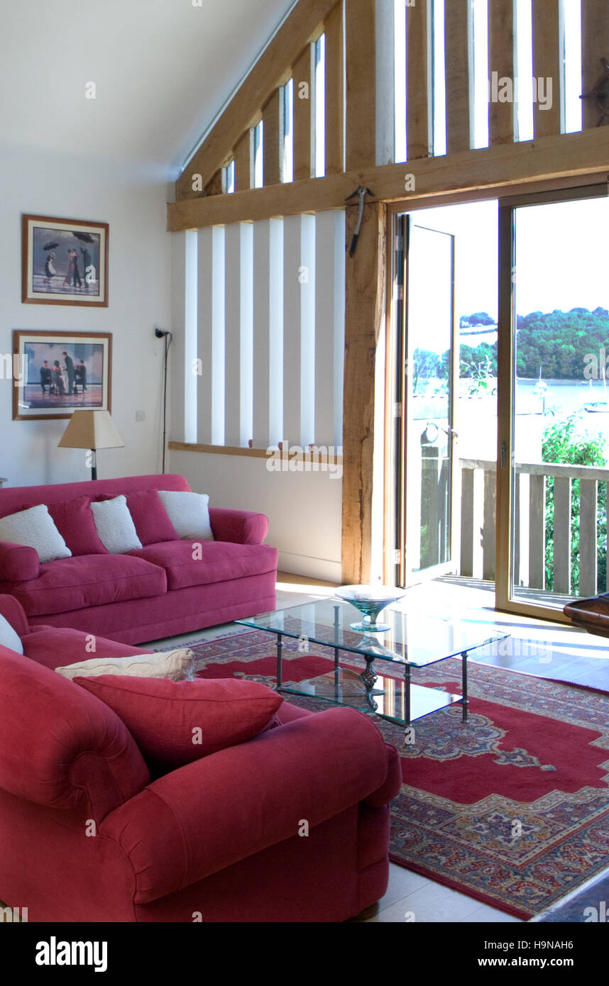 Interior, red sofas, glass doors onto wood balcony, barn conversion, riverside house. Stock Photo