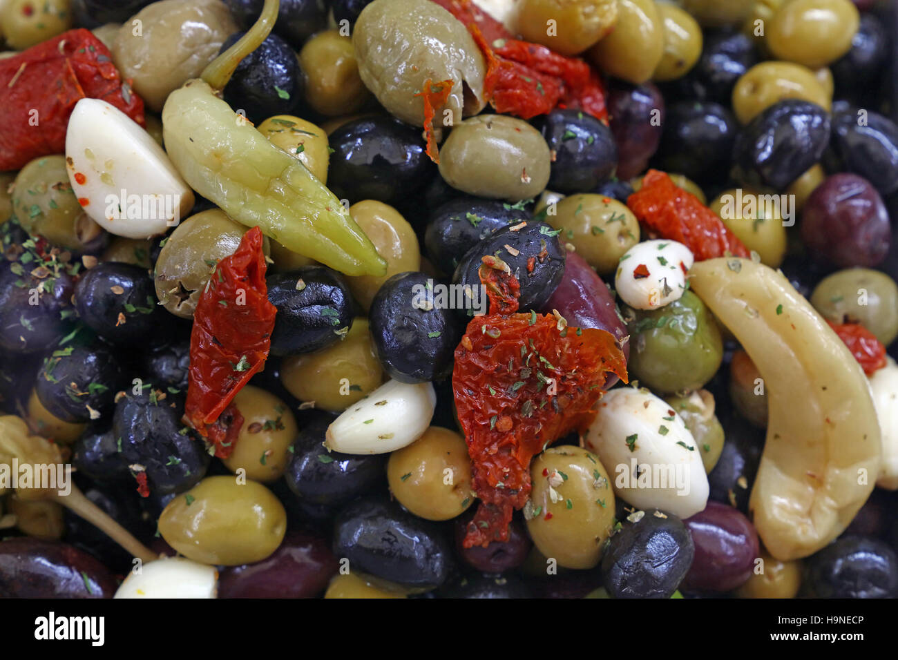 Mediterranean salad mix of assorted whole Italian olives (black, green, red) with garlic, hot pepper and sundried tomato in oil close up, elevated hig Stock Photo