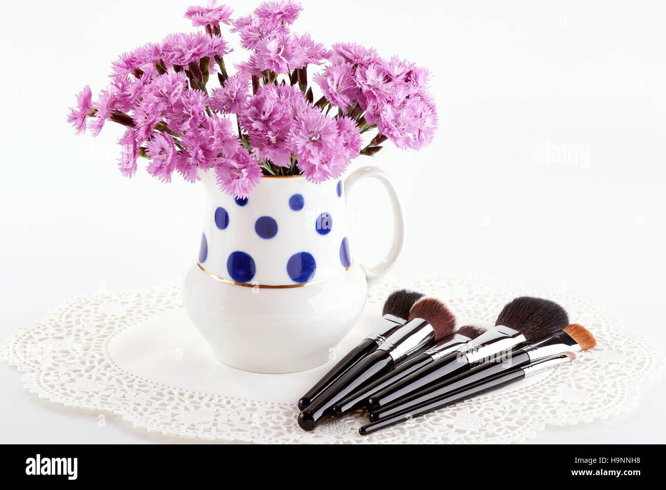 Makeup brushes and flowers in polka dot jug on white background Stock Photo