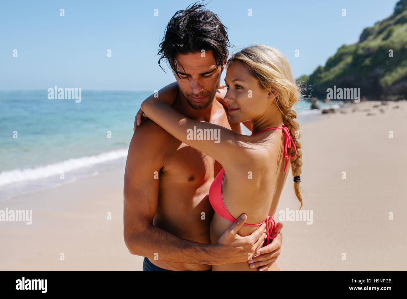 Portrait of romantic young couple embracing on the beach. Beautiful young woman in bikini with her boyfriend on the sea shore enjoying summer holidays Stock Photo