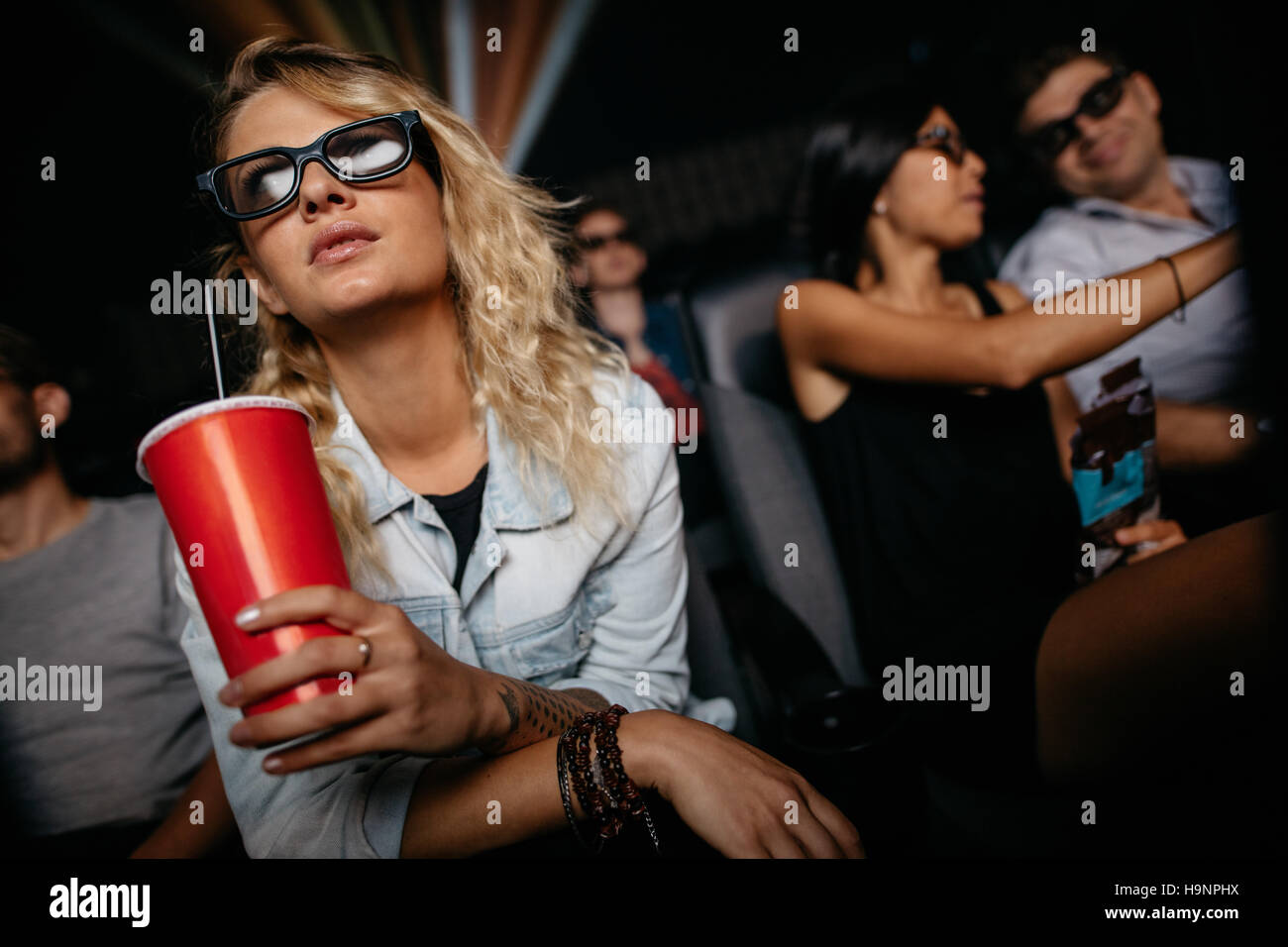 Young woman with cold drink and 3d glasses watching movie in theater