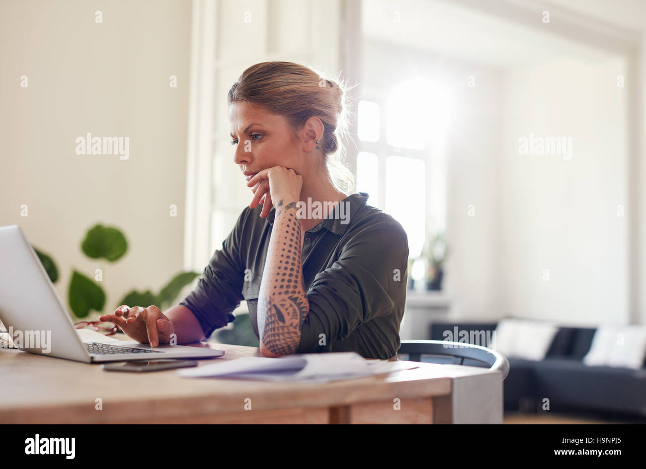 Portrait of beautiful young woman sitting at home office using laptop. Female looking busy working on laptop. Stock Photo