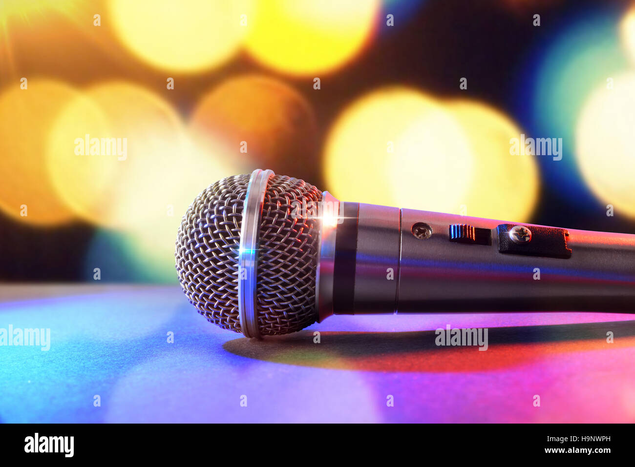 Microphone on black table and colored lights background. Front view. Horizontal composition. Stock Photo