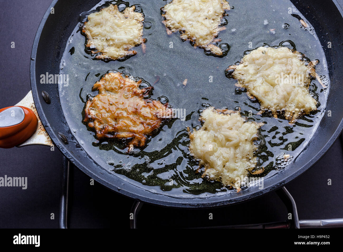 Frying latkes with raw side up and one turned in deep oil on pan on stove from above Stock Photo