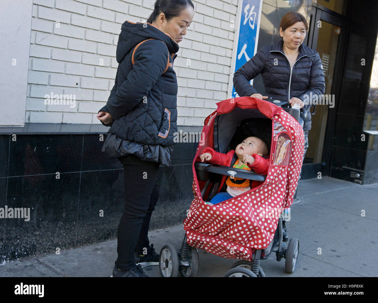 Two Asian women and a responsive child off Main Street in Chinatown, downtown Flushing, Queens, New York City Stock Photo