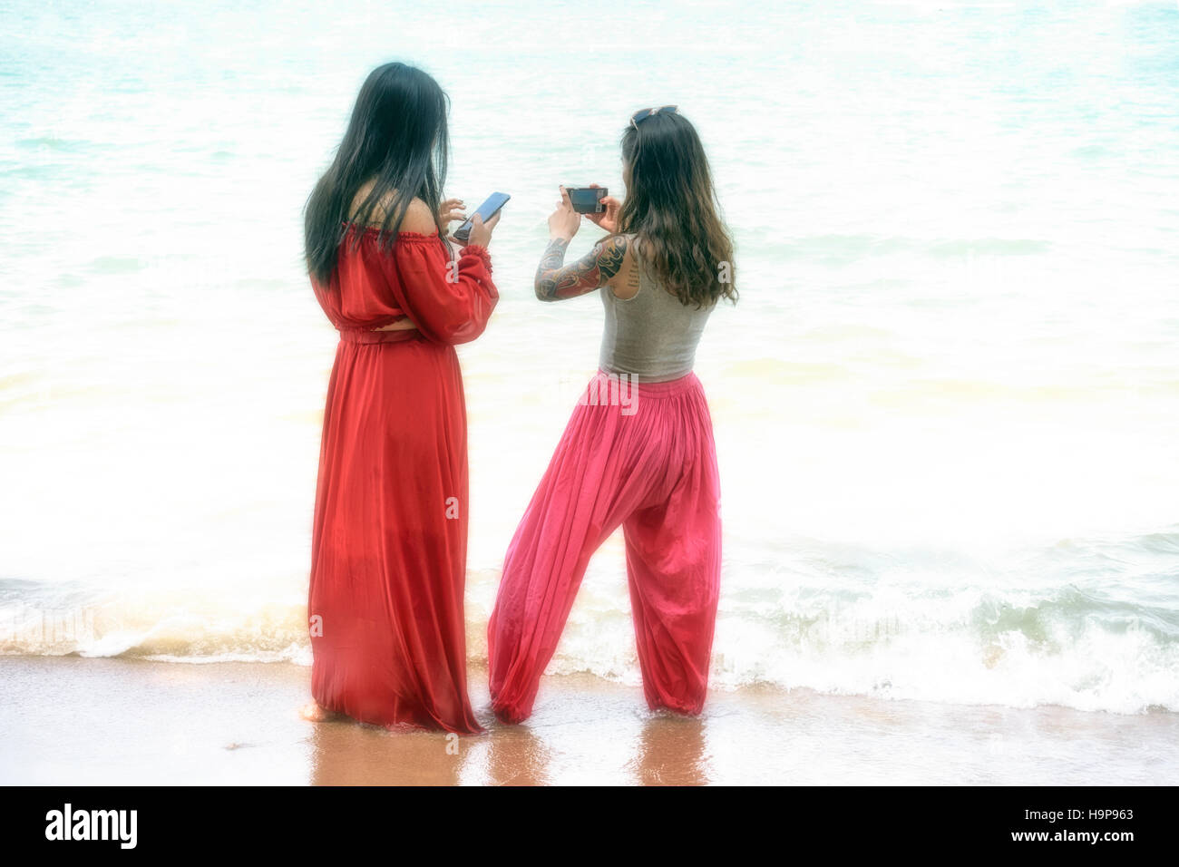 Female friends in red clothes walking in the water at Pattaya Thailand S. E. Asia Stock Photo