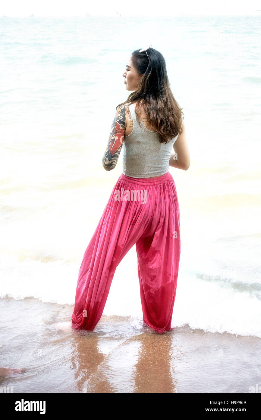 Woman wearing red pantaloon trousers and walking in the sea at Pattaya beach Thailand S. E. Asia Stock Photo