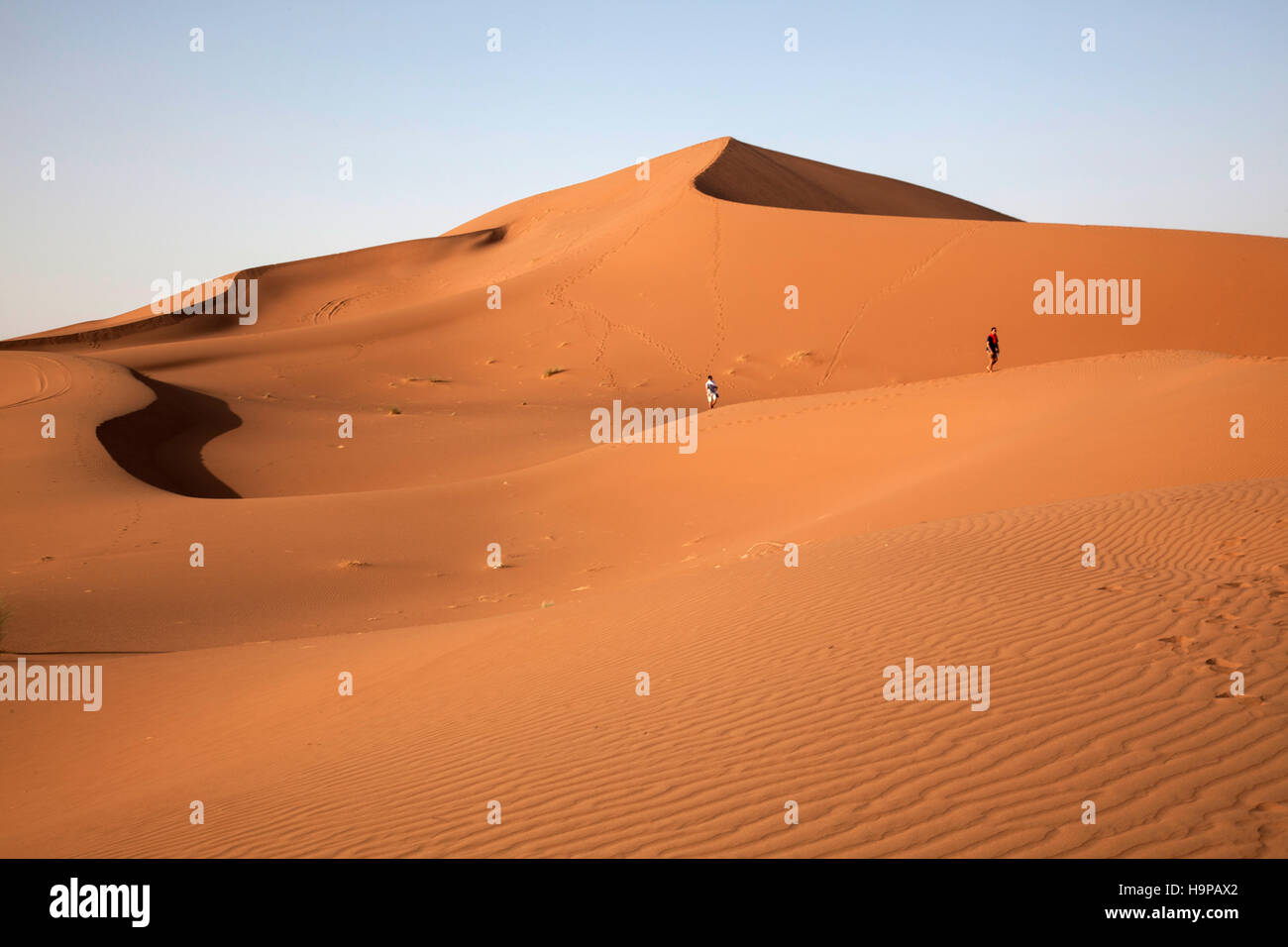 Two boys in the distance walking down a sand dune in the Sahara Desert ...