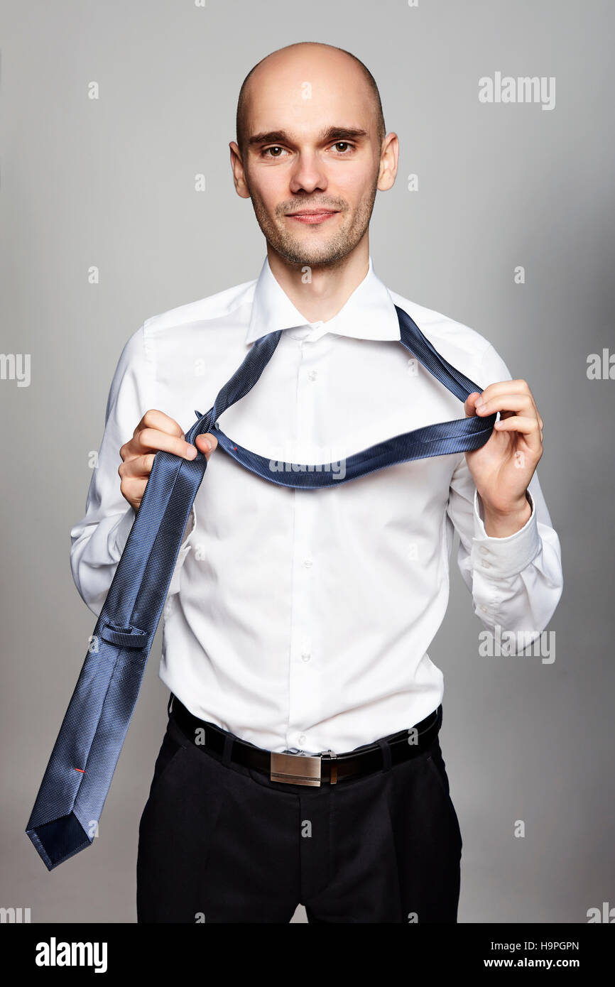 Studio shot of young businessman taking off a necktie. Portrait on gray background. Stock Photo