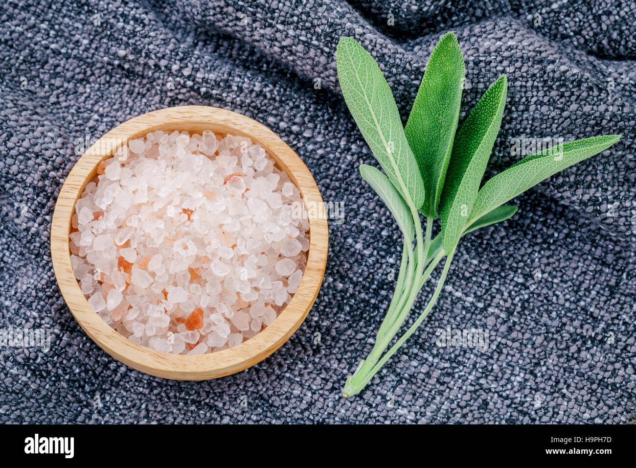 Himalayan pink salt in wooden bowl with sage leaves on dark fabr Stock Photo
