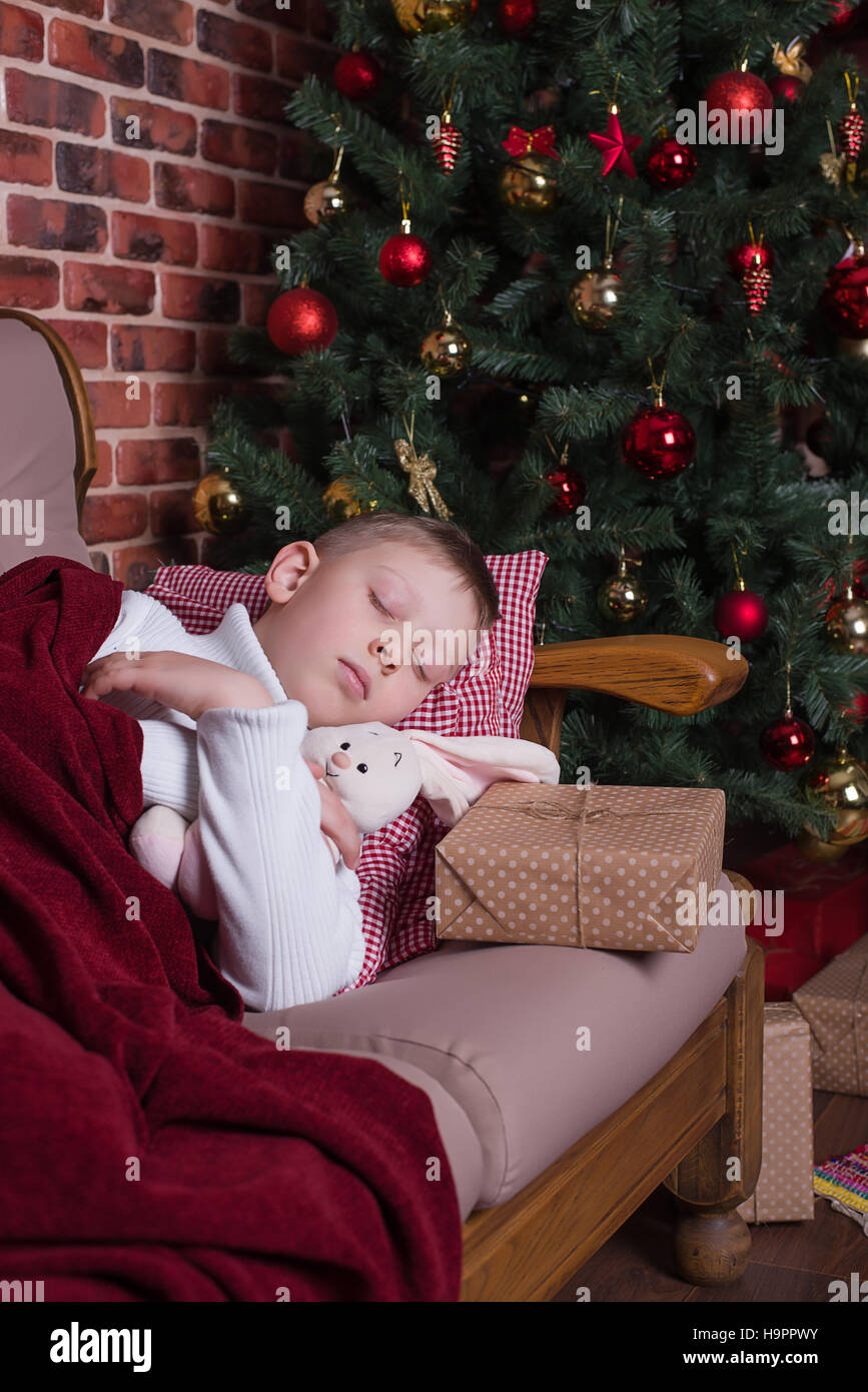 Boy sleeping under a blanket on the sofa near the Christmas tree with