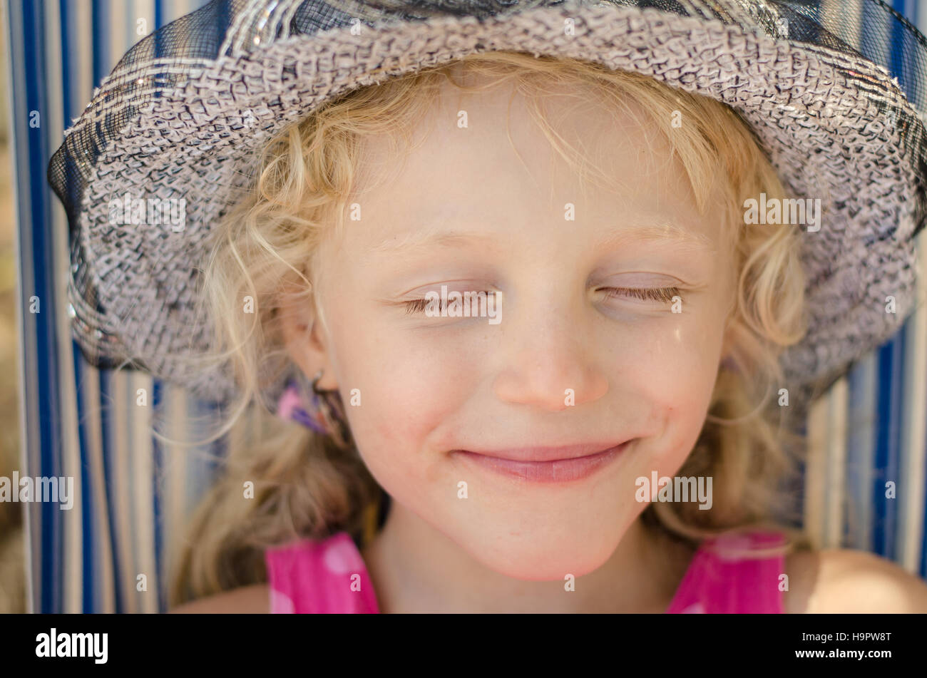 adorable smiling blond little girl with hat and closed eyes portrait