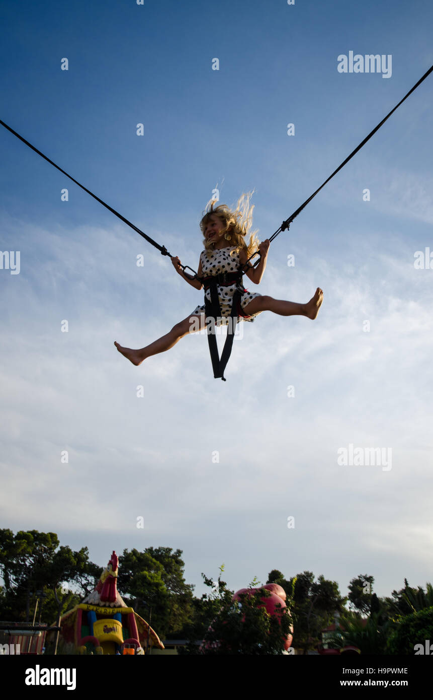 little girl with blowing blond hair jumping into the skies on bungee jumping attraction Stock Photo