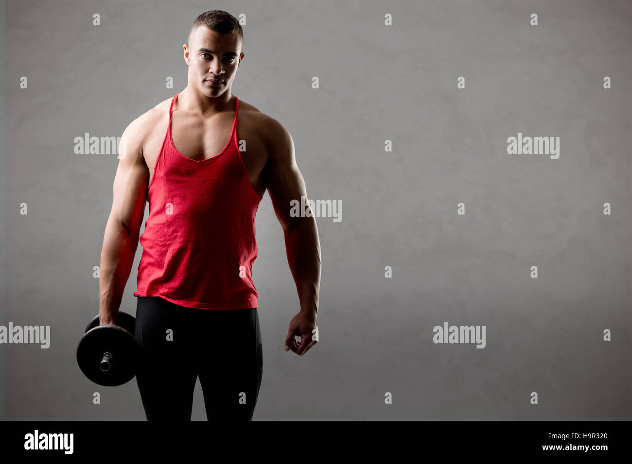 Fit athlete doing standing dumbbell curls for training his biceps, isolated in grey Stock Photo