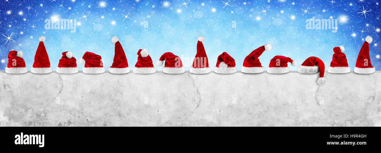 row of red white plush santa claus christmas xmas hat on  empty concrete wall billboard blue bokeh stars sky background Stock Photo