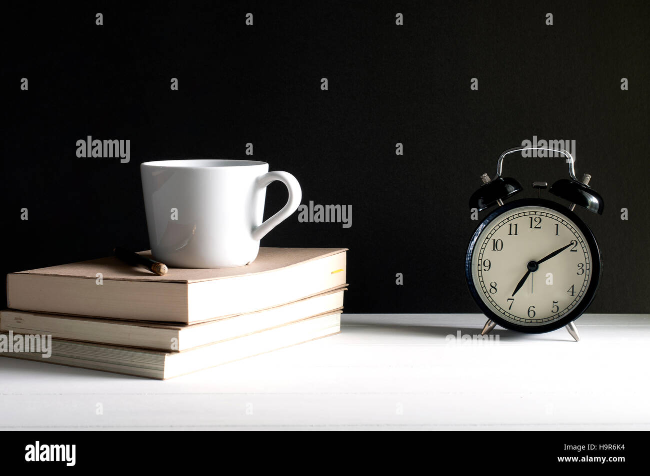 Retro alarm clock beside a cup of coffee on top the books with pencil
