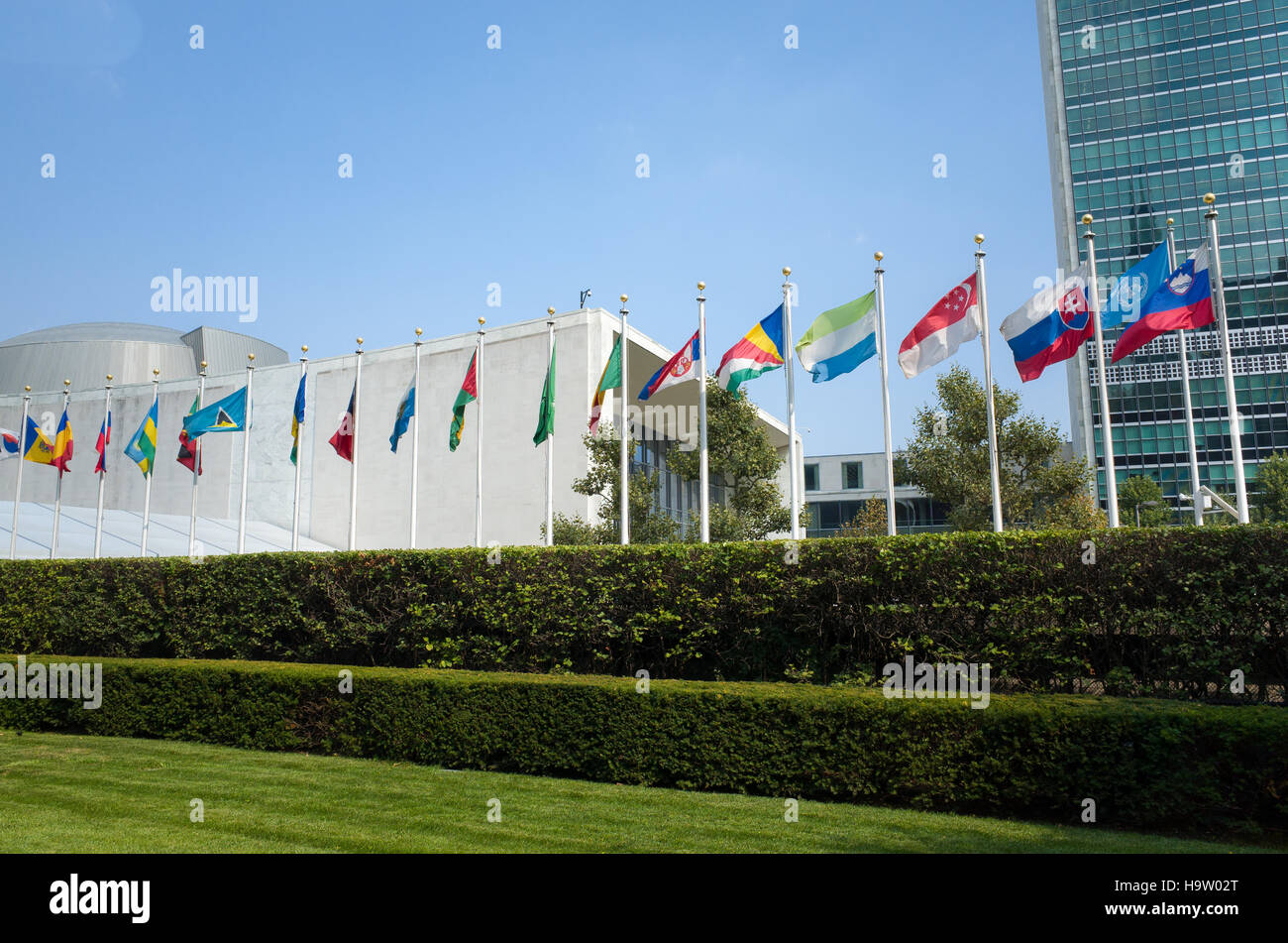 UN United Nations general assembly building with world flags flying in front on a sunny day with blue skies - First Avenue, New York City, NY, USA Stock Photo