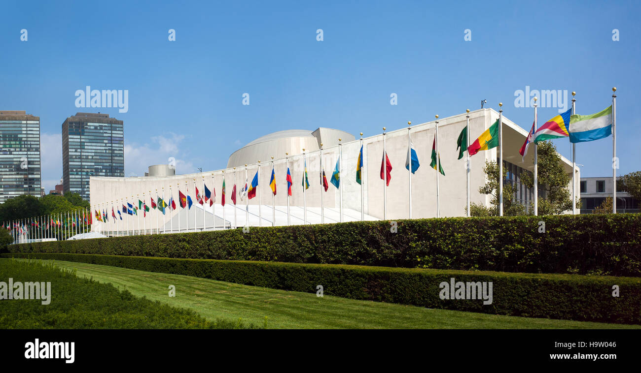 UN United Nations general assembly building with world flags flying in front on a sunny day with blue skies - First Avenue, New York City, NY, USA Stock Photo