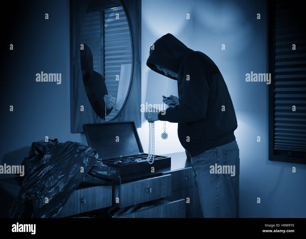 Hooded burglar ransacking a jewelry box in a home Stock Photo