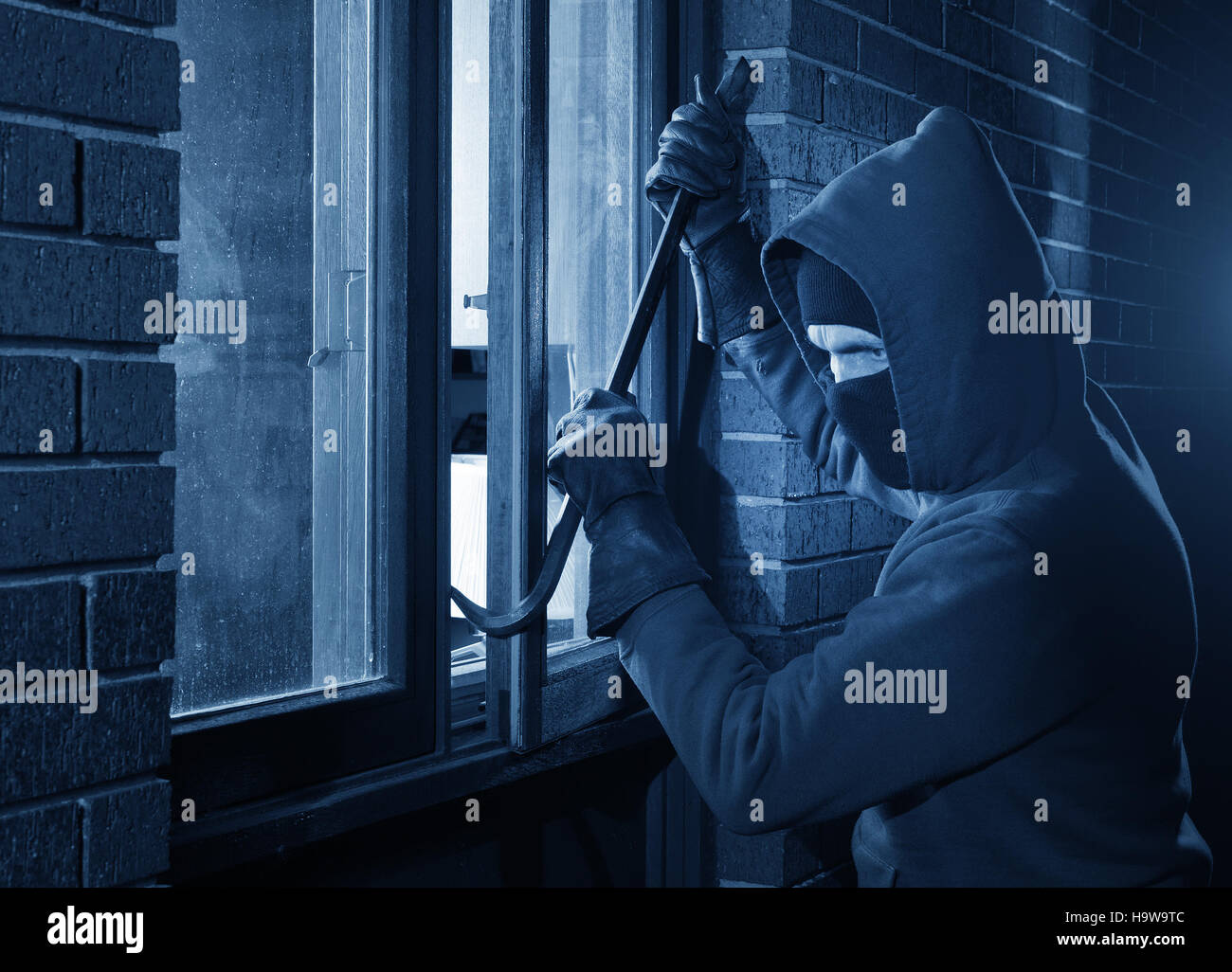 Burglar Using Crowbar To Break Into a House at night Stock Photo