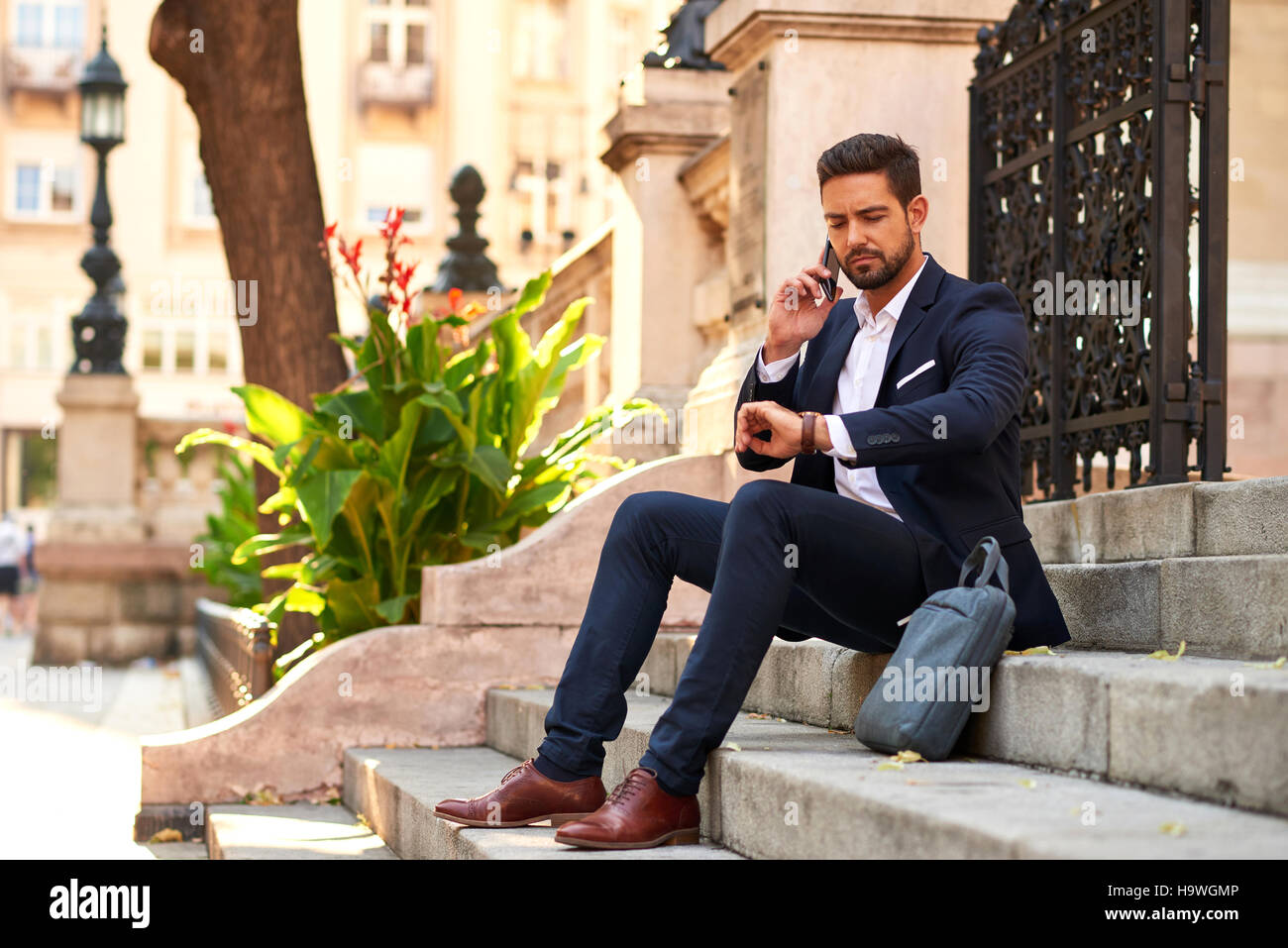 A handsome young businessman sitting on the stairs talking on his ...
