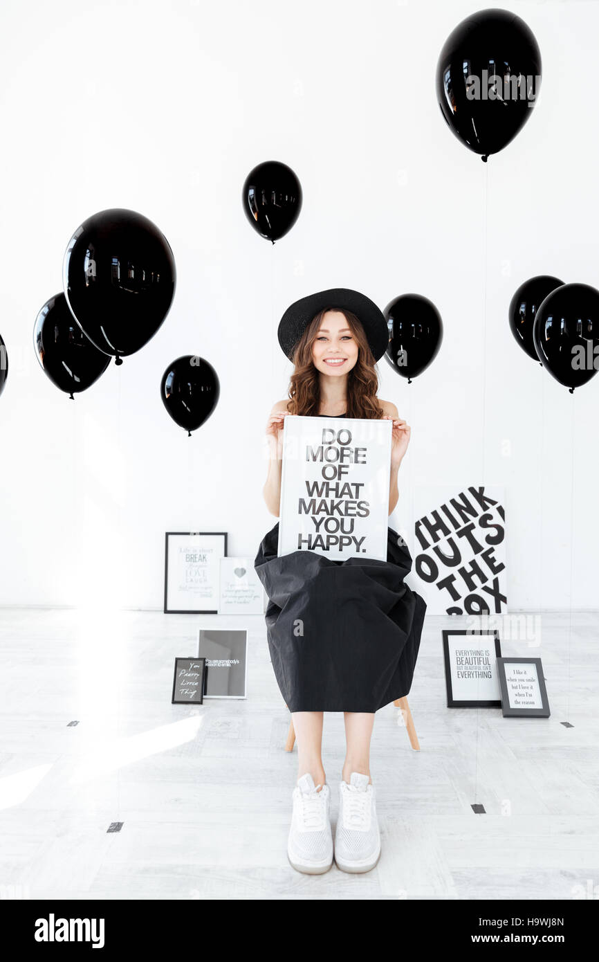 Portrait of cheerful girl with white board over black balloons bakground Stock Photo