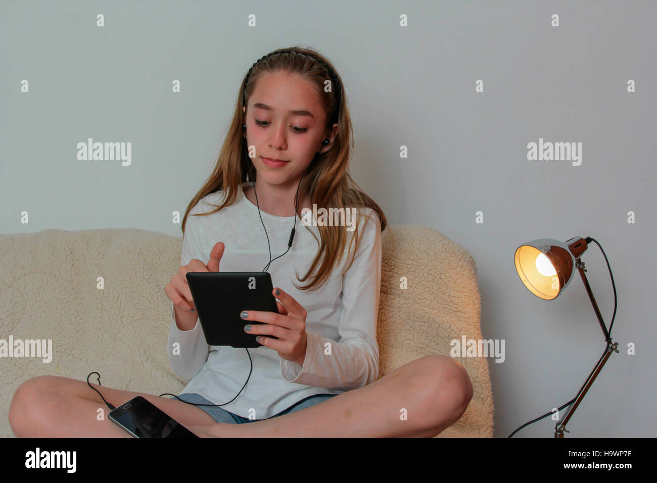 Teenager girl wearing earphone playing on tablet and listening music Stock Photo