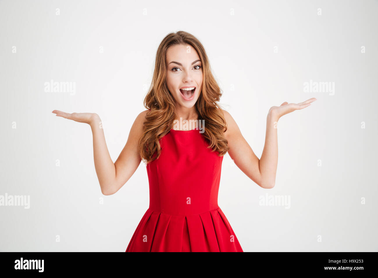 Portrait of a cheerful happy brunette woman in red santa claus dress holding copyspace on two palms over white background Stock Photo