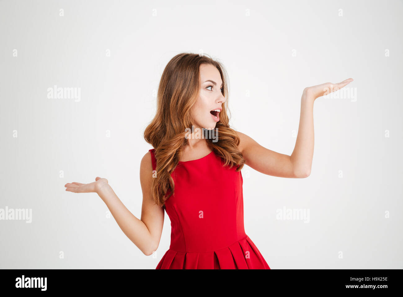 Portrait of a happy young brunette woman in red santa claus dress holding copyspace on two palms over white background Stock Photo