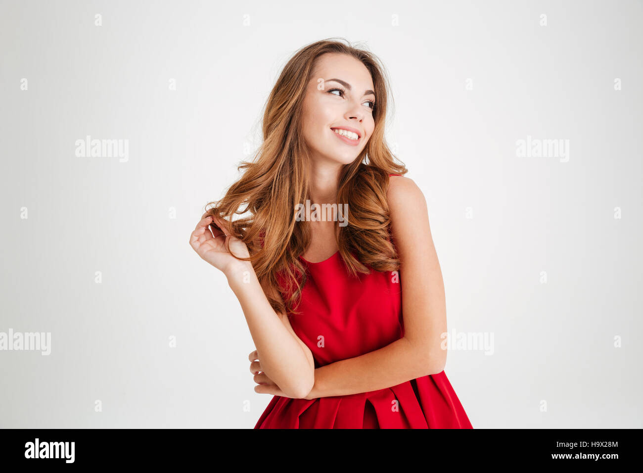 Portrait of a cheerful young brunette woman in red santa claus dress posing and looking away over white background Stock Photo
