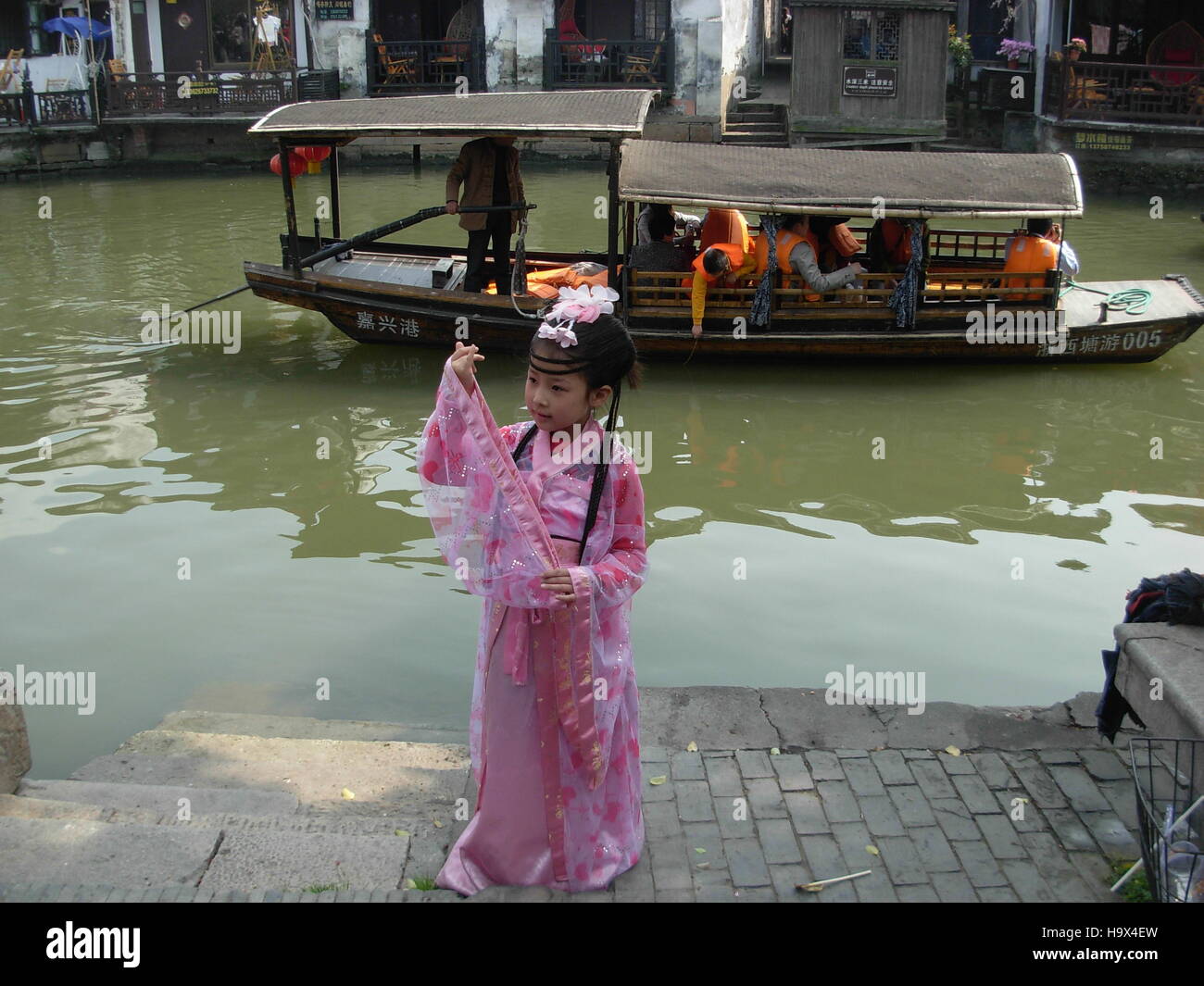 Little chinese child dressed in pink and a boat floating on a river in Xitang water town, Zhejiang province, China Stock Photo