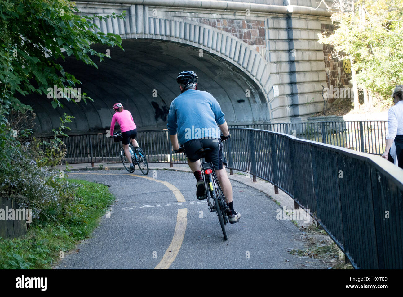 Man and woman riding bicycles under bridge by channel between Lake Calhoun and Lake of the Isles. Minneapolis Minnesota MN USA Stock Photo