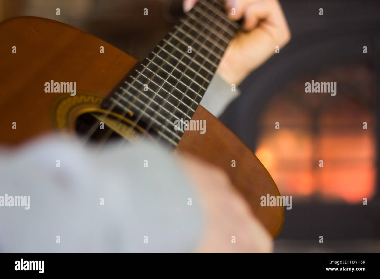 Man playing guitar in front of fireplace Stock Photo
