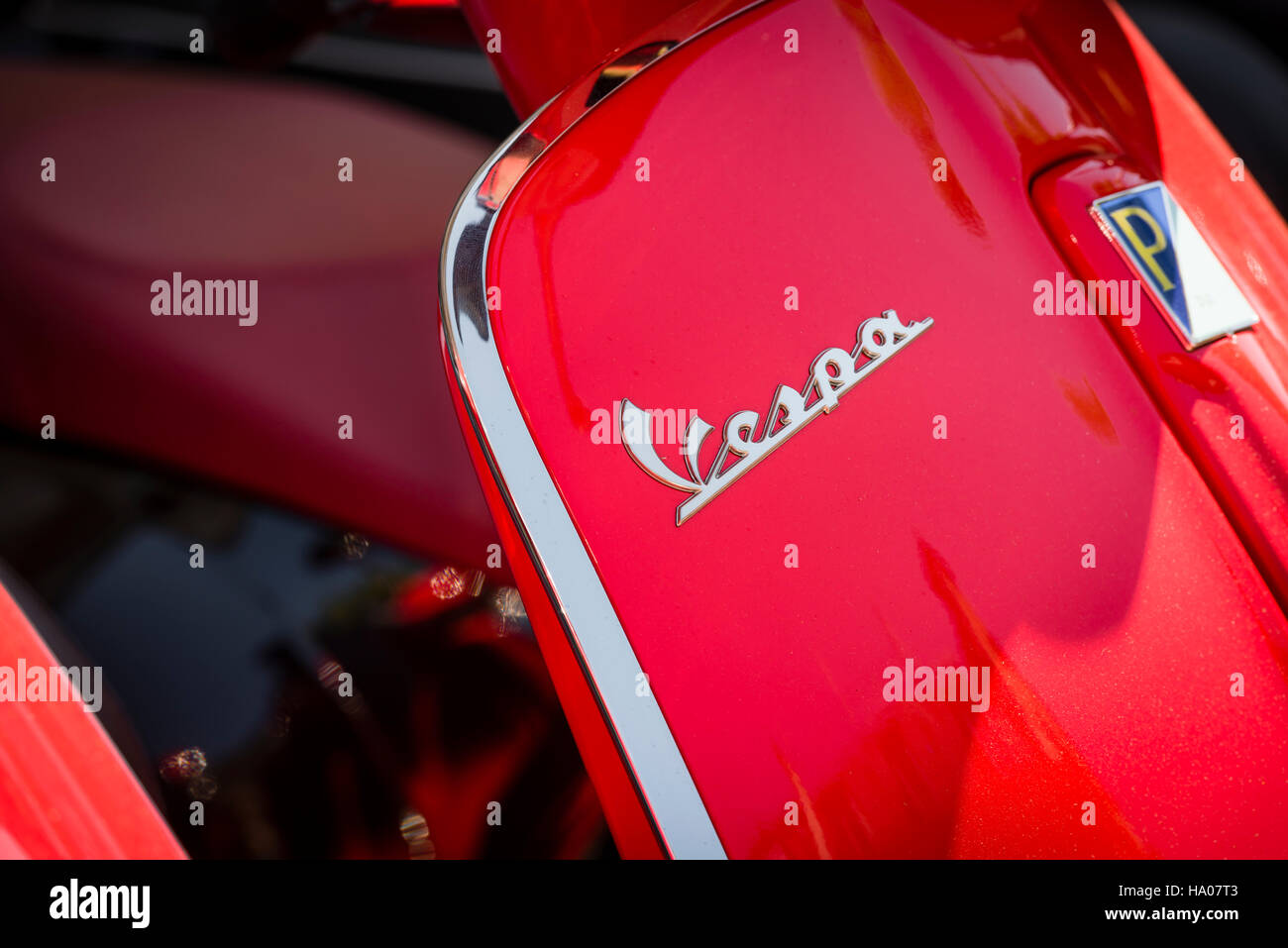 Close-up of the Vespa logo on a bright red Vespa motor scooter parked outside on a street in the sun Stock Photo